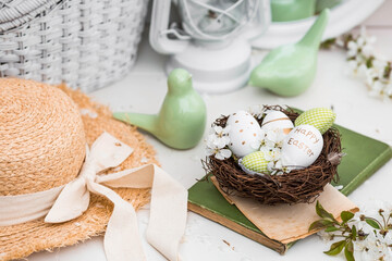 Banner. White-green eggs, cherry blossoms in a nest, an old book and porcelain birds on a white wooden table. A festive card for happy Easter Day 2022 in vintage style.