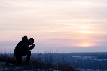 Pray. Repentance. Silhouetted men on a background of blue sky and sunset. Kneeling Prayer to God....