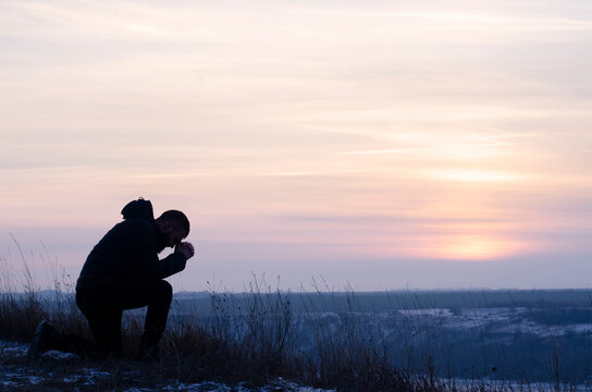 Pray. Repentance. Silhouetted men on a background of blue sky and sunset. Kneeling Prayer to God. Glorification.