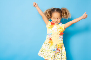 Happy little girl wearing Hawaiian necklace standing isolated over blue background.