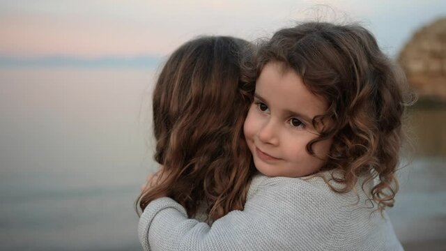 Portrait of a little girl hugging her sister on the beach with sea in the background.
