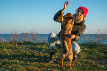 A blonde girl with a purebred dog from the shelter. Playing with a dog on the seashore. Friendship of a dog and a person.