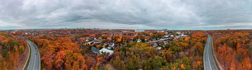 Aerial wide colorful panorama of scenic road in autumnal residential district. Fly above autumn city park with cloudy epic sky. Treetop view on Kharkiv, Ukraine
