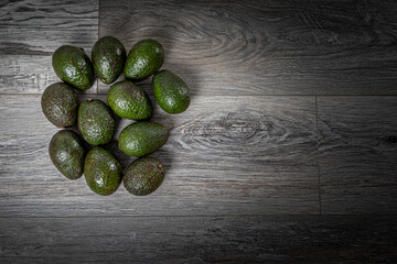 Group of Avocados on a Grey Wood Surface With Circle of Light on the Fruit