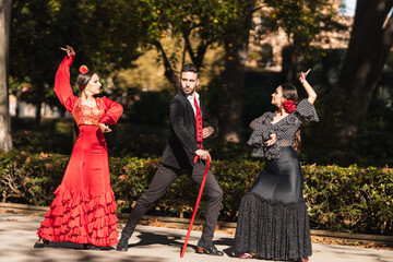 Three hispanic people dancing flamenco next to the gardens of a square - obrazy, fototapety, plakaty