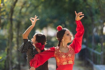 Two women in flamenco traditional costume dancing back to back outdoors - obrazy, fototapety, plakaty