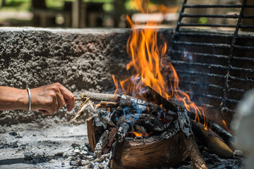 hand placing wood on a campfire, grill on the fire