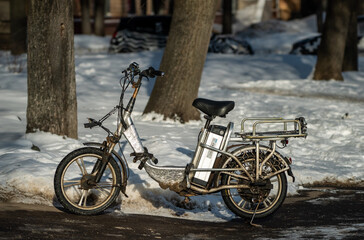 Fototapeta premium Old broken electric bike on the sidewalk in winter.