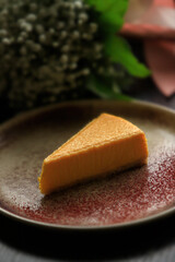 Fruit or vegetable orange cheesecake in a clay plate against the backdrop of a bouquet of flowers.