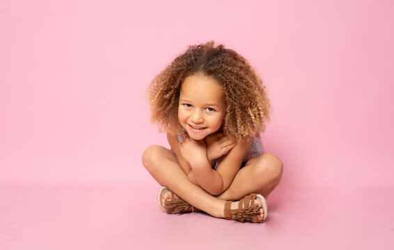 Cute little girl sitting on the floor hugging herself over pink background.