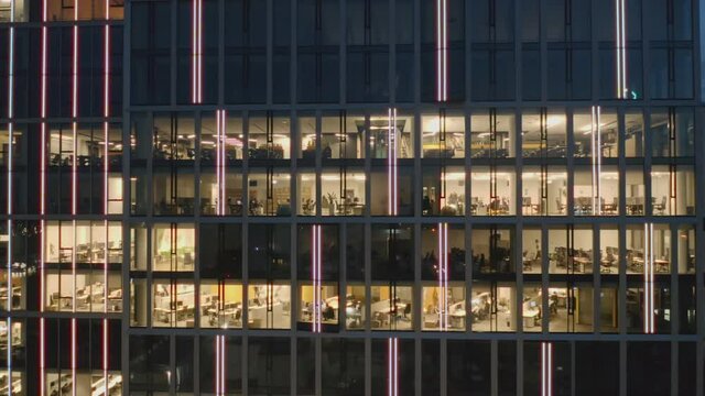Close-up of the windows of a night skyscraper with offices and business people working late at computers aerial view panorama to the right. Camera movement on office windows at night.
