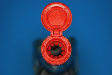 part of glass bottle with soy sauce with open  red plastic cap on blue background