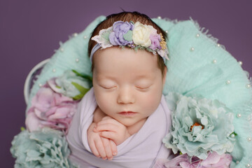 Newborn girl on a purple background. Photoshoot for the newborn. A portrait of a beautiful sleeping newborn baby girl