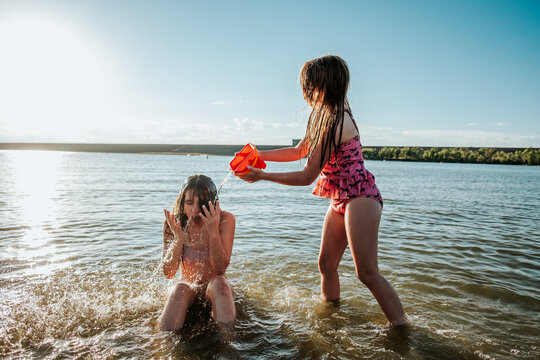 Young Girl Splashing Big Sister With Water In Lake