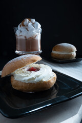 Traditional Finnish foods: Closeup of a sweet shrove bun with whipped cream and strawberry jam filling. A cup of hot chocolate on the side.