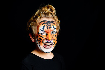 Portrait of a boy with painted tiger face with happy expression, isolated on black background.