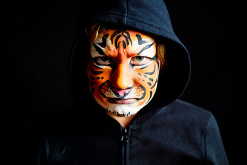 Mysterious look of a child with feline character, painted the face of a dangerous, serious tiger, isolated on black background.