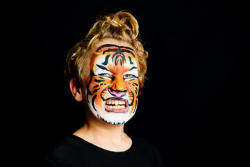 A growling boy with his face painted in the striking colors of a tiger, isolated on a black studio background.