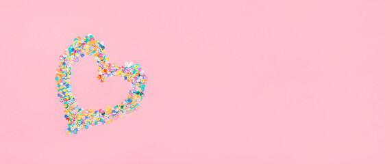 Heart made of multicolored sequins confetti on pink background. Flat festive composition copy space