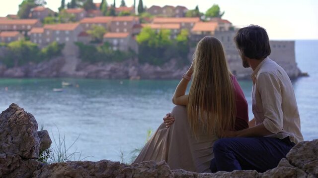 A man and a woman travelers visit the Sveti Stefan island. Famous tourist location near the city of Budva. Travel to Montenegro concept. - Powered by Adobe