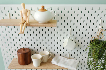 Peg board with dishes, wooden mannequin and houseplant hanging on green wall