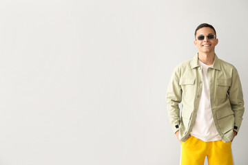 Young man in stylish sunglasses and jacket on light background