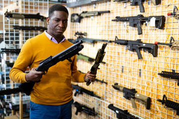 Portrait of active african american man choice pneumatic gun in airsoft market