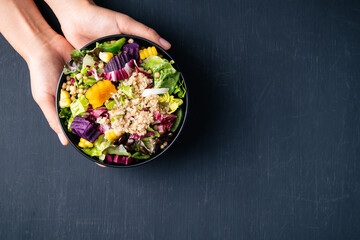 Fresh organic vegetables salad with quinoa seed in bowl holding by hand on black background, Healthy Vegan food, Top view