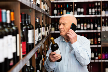 Senior man chooses wine and consults on a cell phone