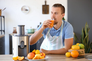 Young man with glass of fresh fruit juice near modern juicer in kitchen