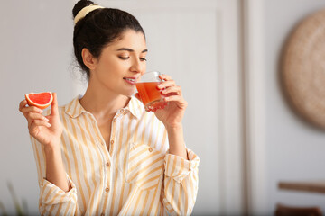 Young woman drinking fresh grapefruit juice in kitchen