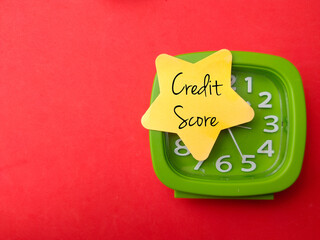 Alarm clock with colored sticky note with text Credit Score on red background.