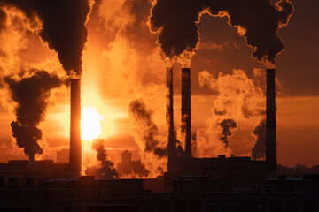 Chemical factory chimneys with raising smoke against red sunset sky in winter city during strong...