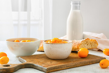 Bowl of tasty kumquat jam, bread and fresh fruits on kitchen table