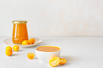 Jar and bowl of tasty kumquat jam and fresh fruits on light background