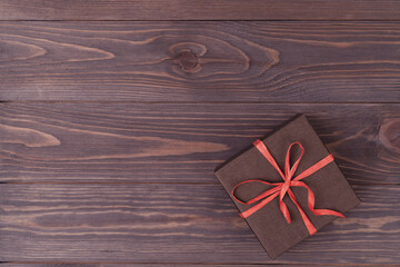 brown wooden background with a gift box packed in brown paper and tied with a red ribbon, lilac...