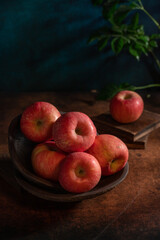 The apples on the plate look like oil paintings under the dim light on the wood grain table