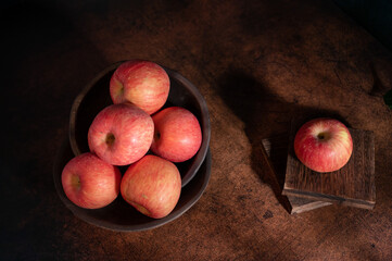 The apples on the plate look like oil paintings under the dim light on the wood grain table