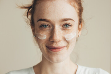 Closeup portrait of woman face with cream on cheek. Caucasian woman with red hair, clean fresh...
