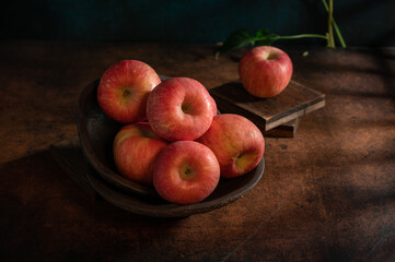 The apples on the plate look like oil paintings under the dim light on the wood grain table