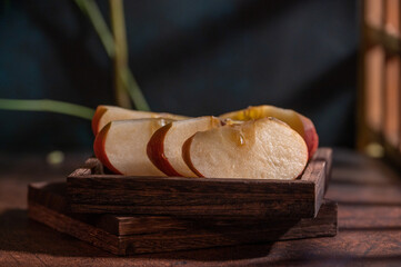 The apples on the plate look like oil paintings under the dim light on the wood grain table