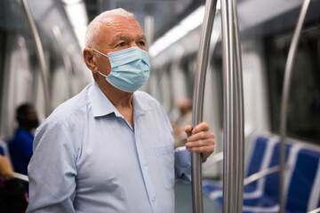 Fototapeta na wymiar Old man in face mask standing in subway car and holding handrail.