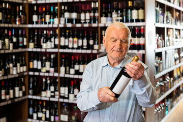 Attentive pensioner chooses red wine in a liquor store. High quality photo