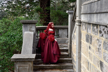  portrait of pretty  female model with red hair wearing glamorous renaissance red ballgown.  Posing...