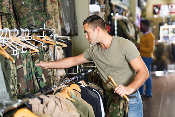 Caucasian man selecting outwear in military goods store. African-american man making purchases in...