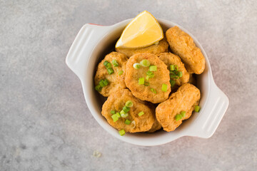 Golden chicken nuggets in a plate, sprinkled with green onions and a lemon wedge. Copy space. Flatlay
