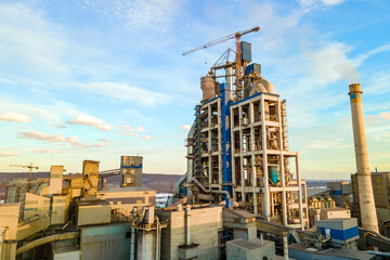 Aerial view of cement plant with high factory structure and tower crane at industrial production area at sunset