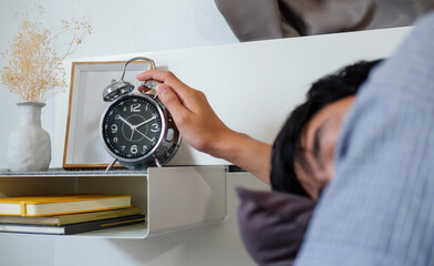 Young man lying on bed and turning off the alarm clock wake up at the morning.