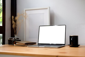 Computer laptop, picture frame and coffee cup on wooden table.