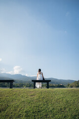 Woman in white dress sitting on seat at hill and blue sky on sunny day